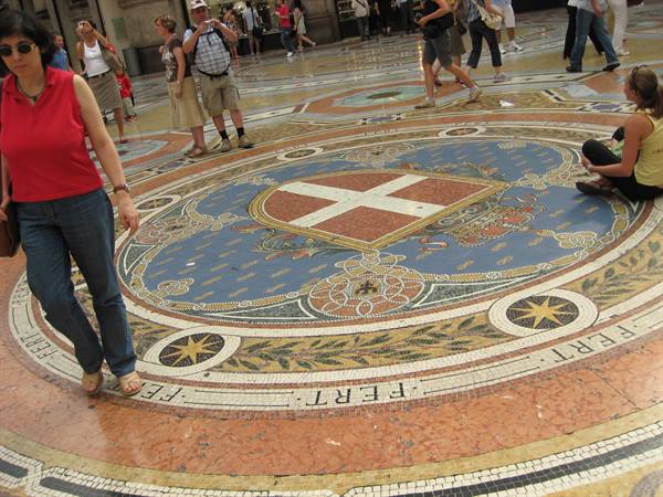 Tourists walk over the Savoy coat-of-arms mosaic in Galleria Vittorio Emanuele II