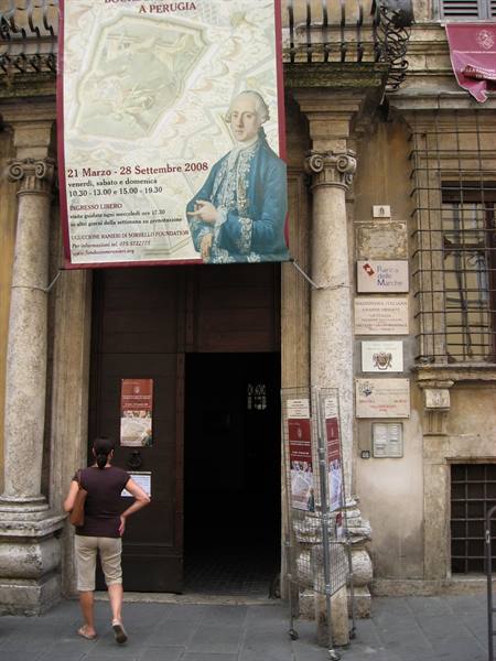 Woman at a palace entrance in Perugia beneath a large historic exhibition banner