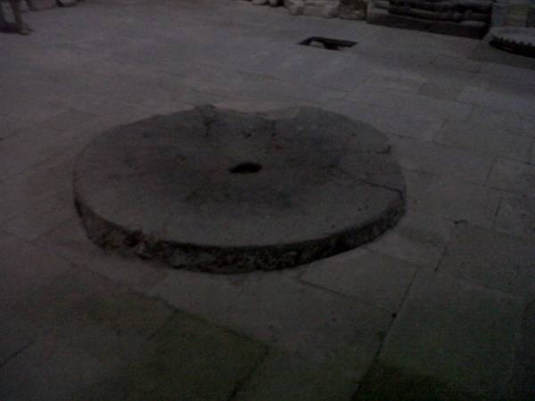 Ancient round stone millstone embedded in the paved floor, dim light
