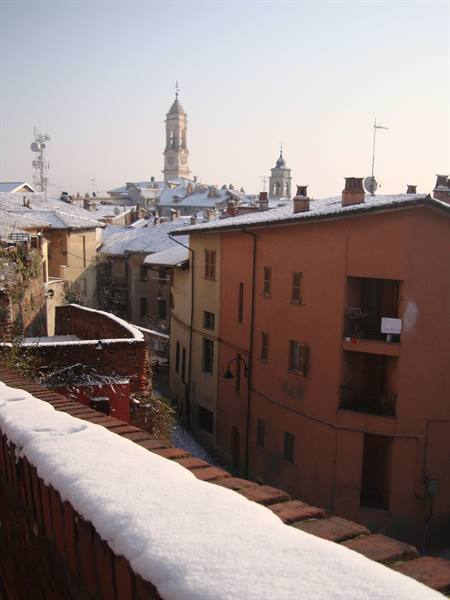 Snow-covered roofs of ochre houses beneath Modena's bell tower