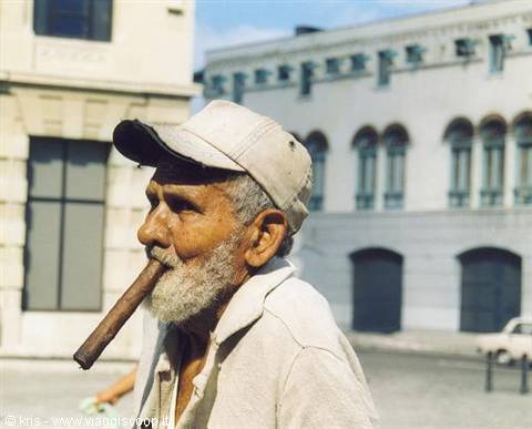 Elderly man in cap smoking a large cigar by colonial building