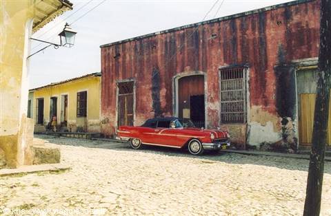 Vintage red car parked beside crumbling colonial facade, Trinidad