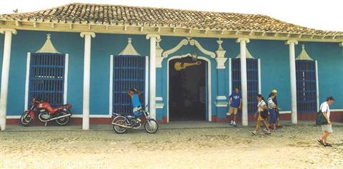 Tourists walk past a blue colonial house with parked motorcycles