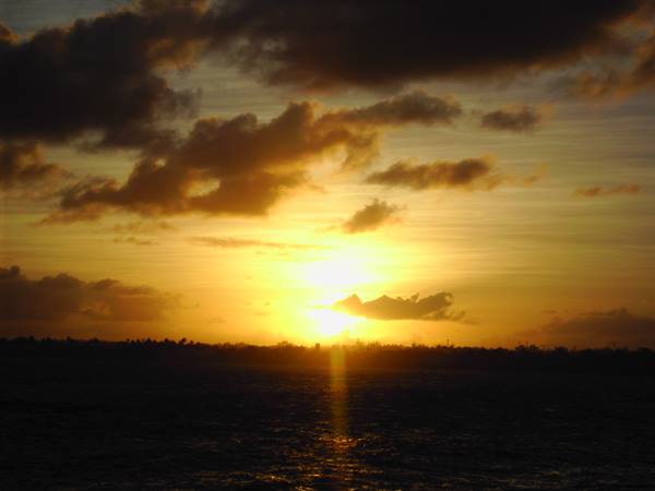 Low sun glowing through clouds above dark water at the horizon