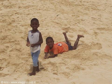 Two smiling children on a golden sandy beach, one lying on his stomach
