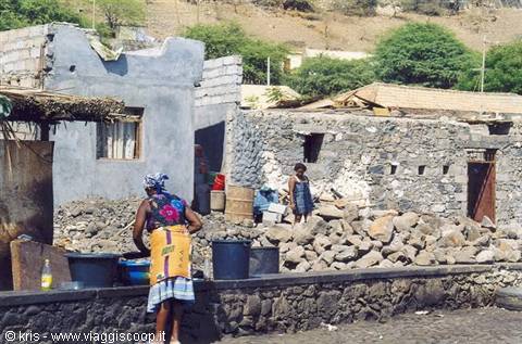 Woman in colorful dress with buckets beside stone and concrete houses