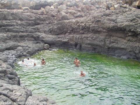 Swimmers in a natural pool carved into dark volcanic rock