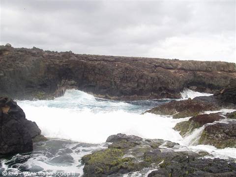White waves crashing on black lava rocks, gray sky