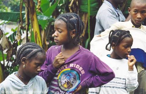 Children with braided hair among banana plants, one in purple sweatshirt