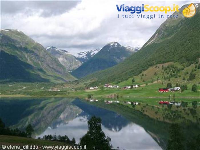 Red farmhouses and green meadows reflect in the lake beneath snowy mountains