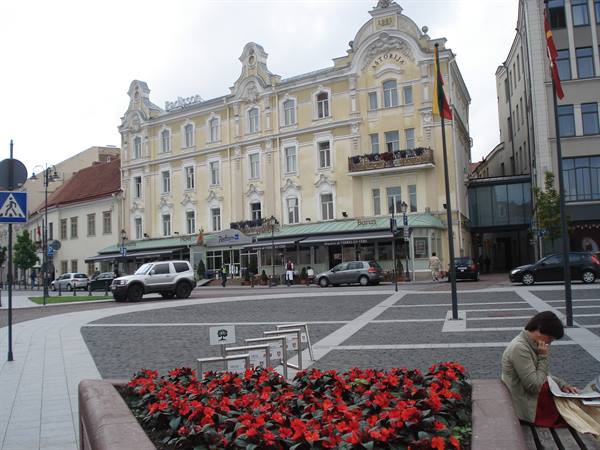 Square with yellow Art Nouveau building, red flower bed, woman sitting on bench
