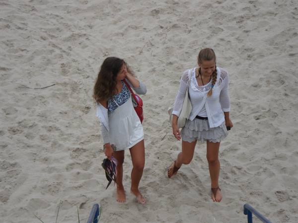Two barefoot girls in white dresses walking on the beach sand