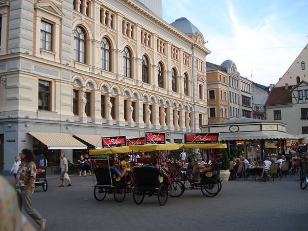 Pedal rickshaws parked by outdoor cafés on Riga square