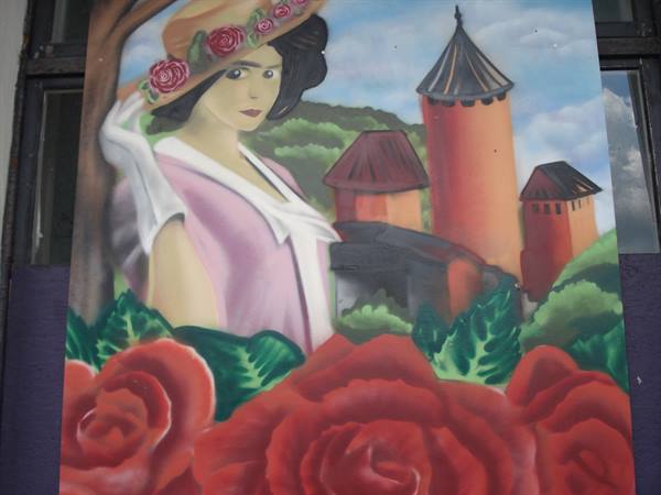 Painted mural: woman in flowery hat beside red towers and roses