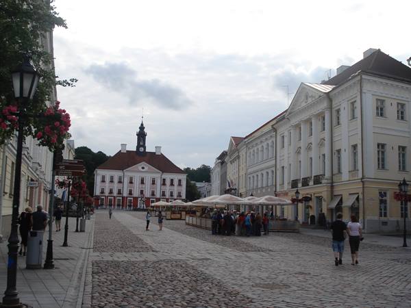 Tartu Town Hall Square, yellow classical buildings, white kiosks, tourists on cobblestones