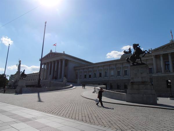 Tourist walks past the Vienna Parliament, bronze equestrian statue under bright sun