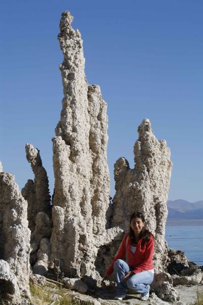 Woman crouching beside tall tufa limestone formations, lake and mountains in the background