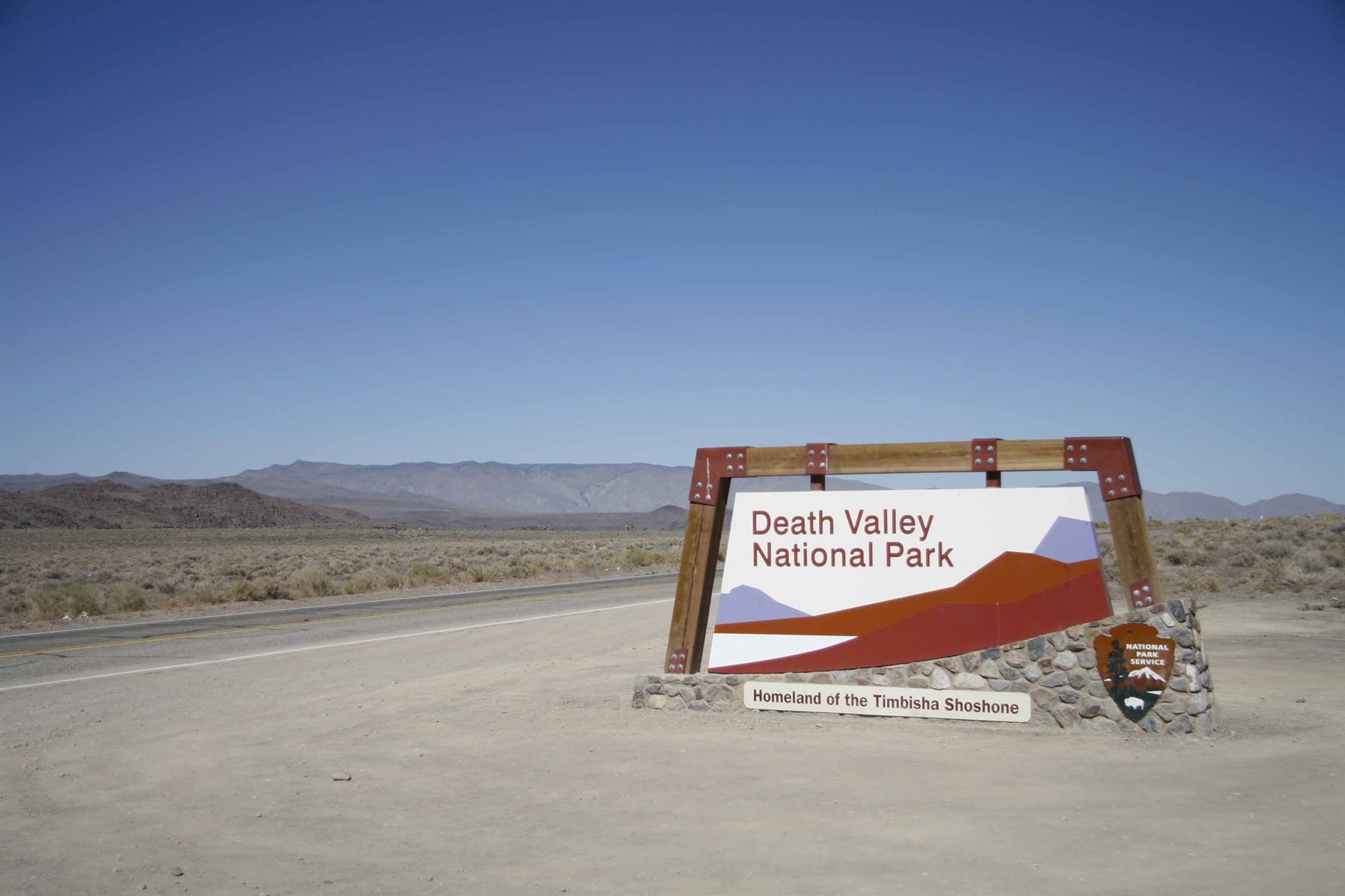 Wooden and stone entrance sign of Death Valley National Park by desert road