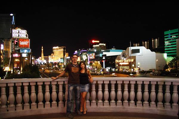 Couple on a stone balustrade, illuminated Las Vegas Strip at night with neon signs
