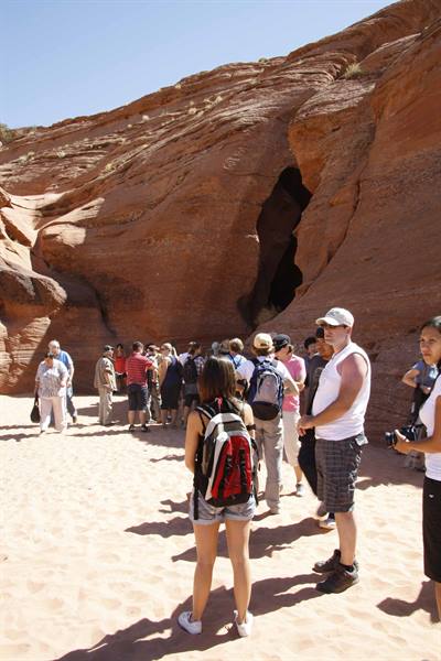 Tourists with backpacks at Antelope Canyon, red sandstone walls under the sun