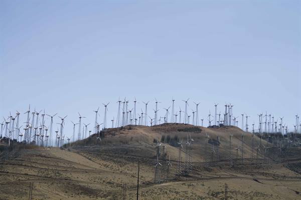 Many white wind turbines on dry hill under blue sky