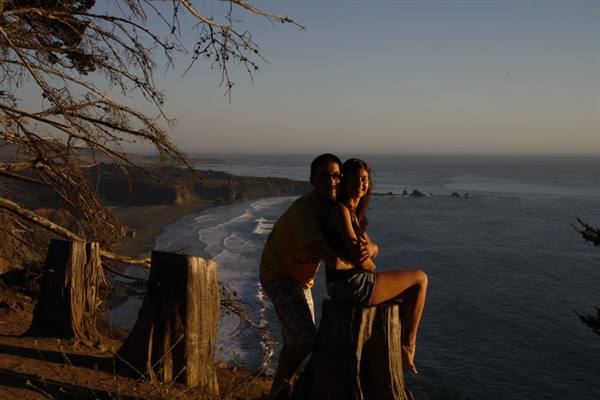 Couple sitting on a cut trunk, ocean and beach bathed in golden light
