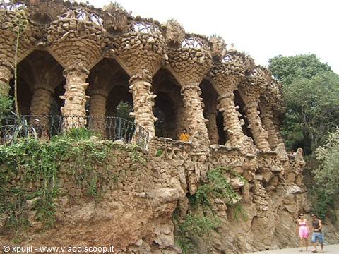 Stone colonnade of Gaudí's Park Güell in Barcelona, tourists walking nearby