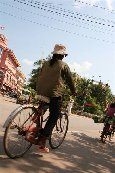 Woman in a hat pedals an old bicycle on a sunny Phnom Penh street