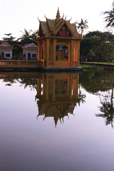 Golden Buddhist pavilion reflected in pond, palm trees, soft morning light