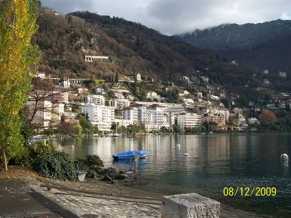 Blue boat moored on Lake Maggiore shore, hotels on hillsides above Locarno