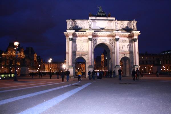 Arc de Triomphe du Carrousel at the Louvre, lit up at night among passersby