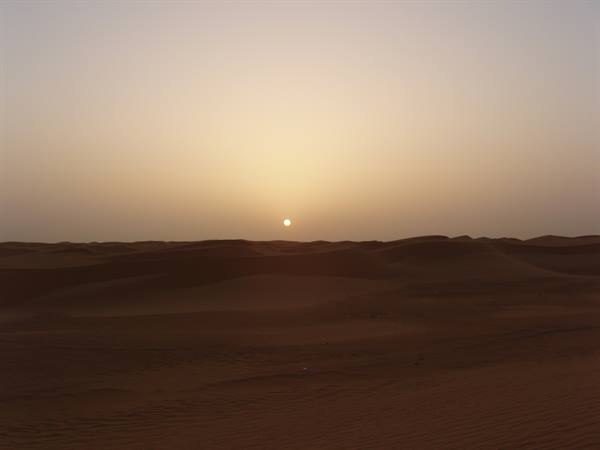 The low sun glows over the sand dunes of the desert
