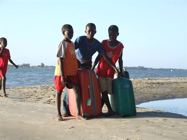 Boys with red and green suitcases on a sunlit sandy beach