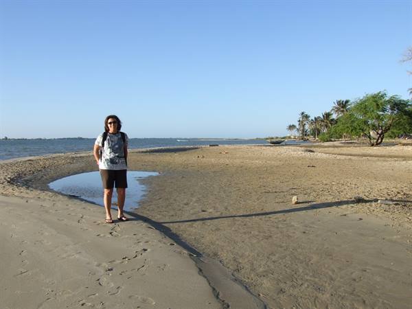 Woman with backpack on sand next to a tidal pool and palm trees