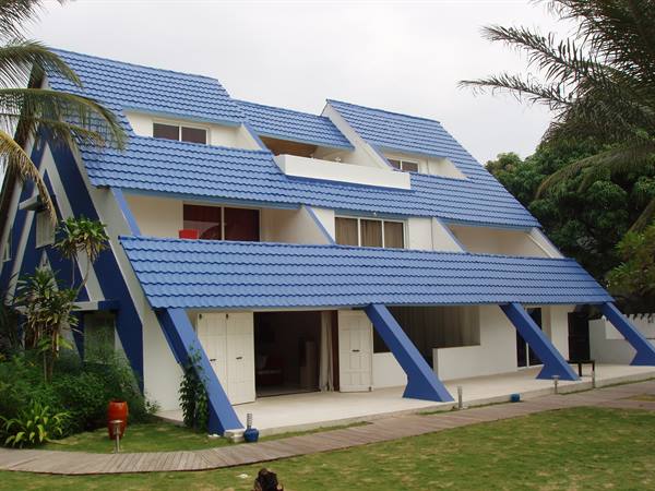 White villa with stepped blue-tiled roofs among palm trees and green lawn