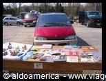 Red van parked behind a table of used books and DVDs for sale