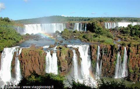 Rainbow over Iguazú Falls among red rocks and lush greenery