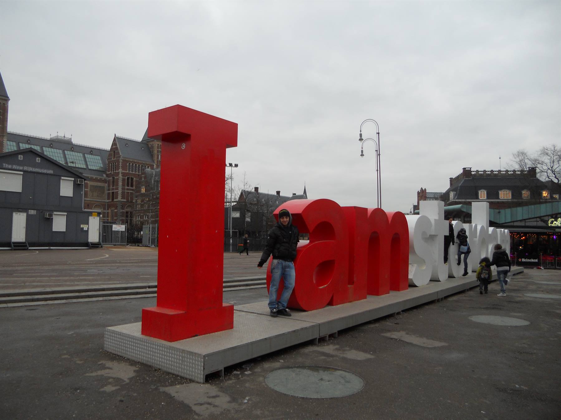 Tourist next to the I Amsterdam letters on a square, grey sky