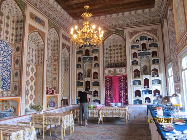 Hall with tiled niches of porcelain, golden chandelier, woman setting breakfast tables