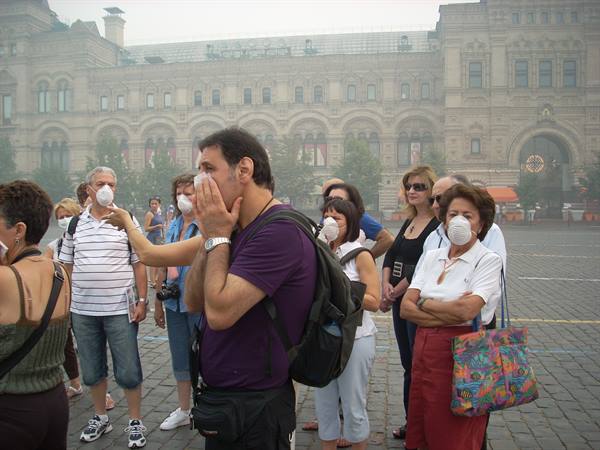 Masked tourists on Red Square amid smog, historic GUM building behind