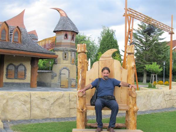Man sitting on a large wooden chair in a park with fairy-tale style houses