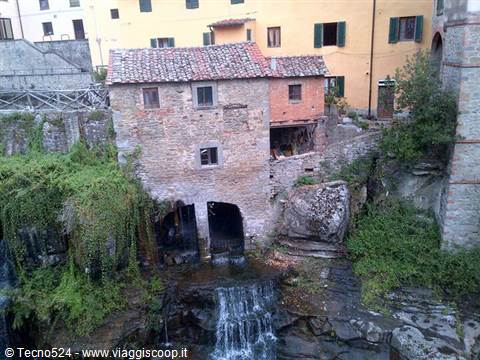 Old stone mill above a small waterfall, colorful houses behind