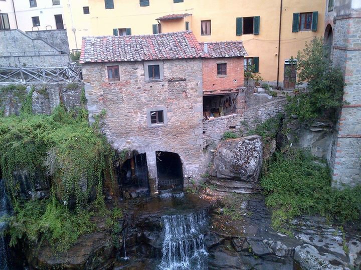 Vecchio mulino in pietra sopra una cascata, case colorate sullo sfondo
