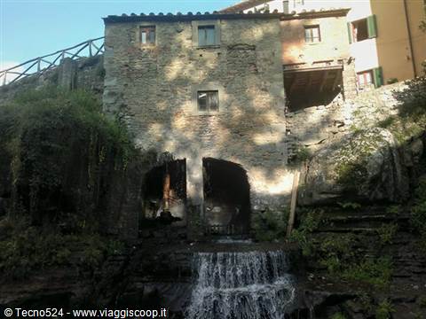 Old stone mill with arches above a small waterfall