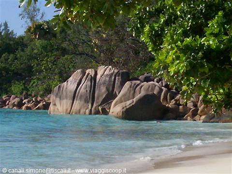 Large granite boulders between turquoise water and white sand, tropical vegetation