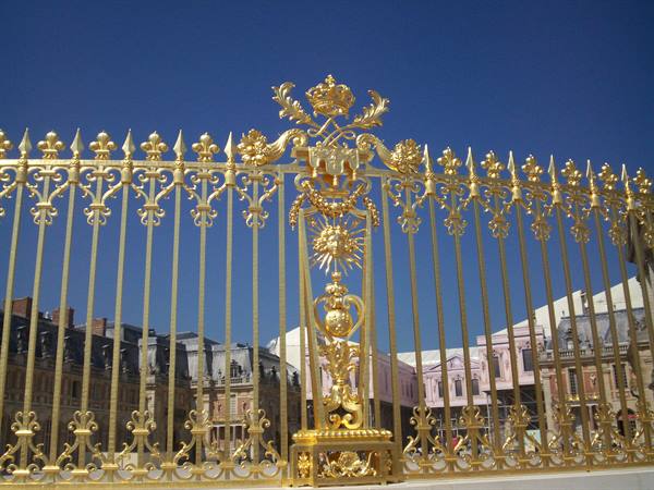 The golden gate of Versailles shines under a blue sky