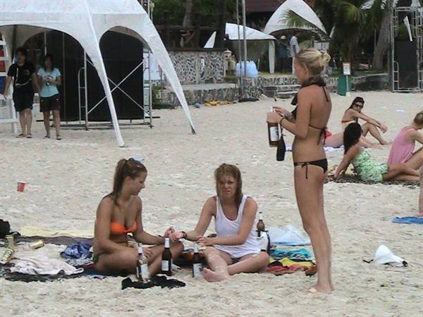 Women in bikinis drink beer on the sand, white tent behind
