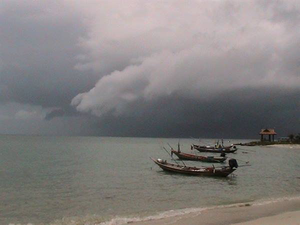 Thai longtail boats moored at the shore beneath dark storm clouds