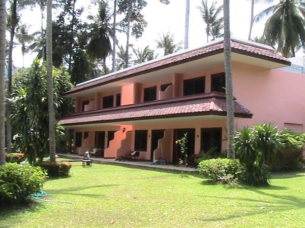 Two-story pink hotel with tiled roofs among palm trees and green lawn