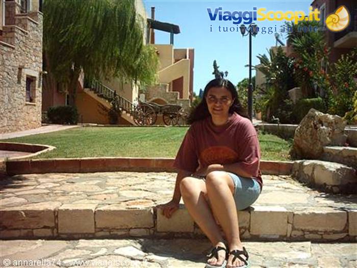Smiling woman sitting on stone steps among sunny buildings and garden